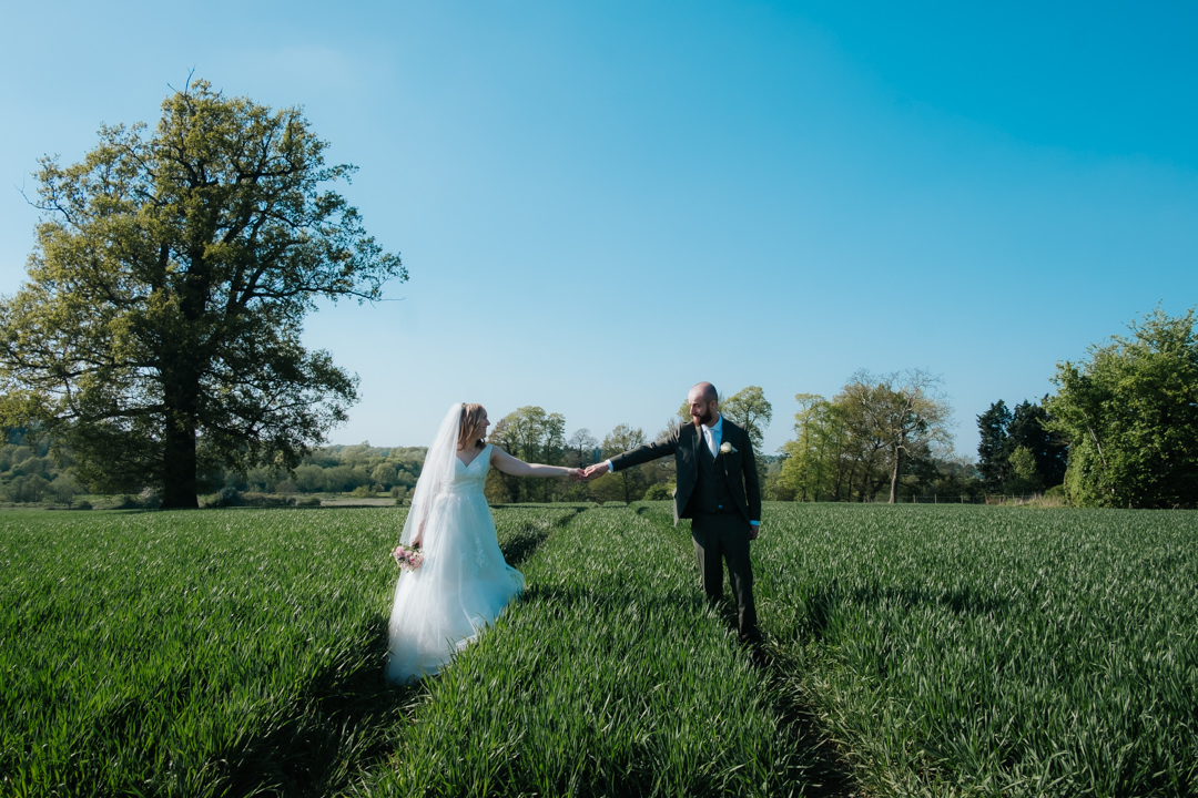 Bride and groom holding hand in the cornfeilds on their way to the Saxon Mill for their wedding reception after getting married at Old Milverton church