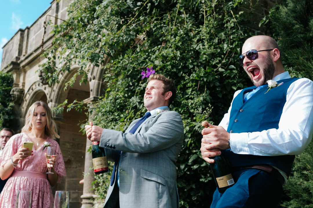Ushers pop champagne corks during wedding reception drinks at Nymans Garden Wedding