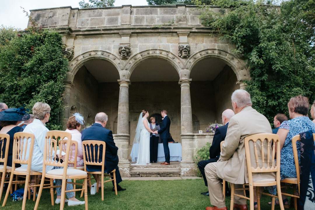 bride and groom stand inside stone columns in their Nymans Garden Wedding ceremony