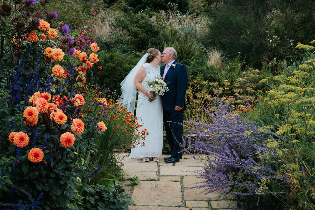 Father of the bride and the bride share an embrace in the beautiful gardens of Gravetye Manor wedding venue