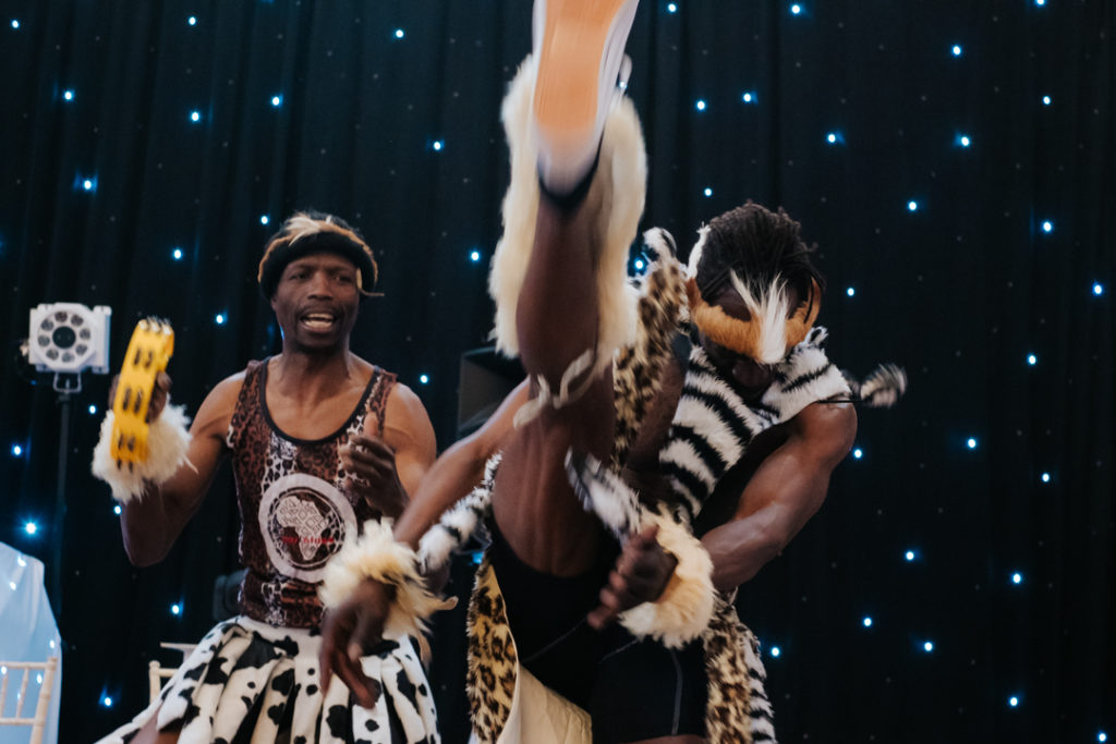 male African dancer kicks his leg above hishead in impressive dance at Worton hall fusion wedding party