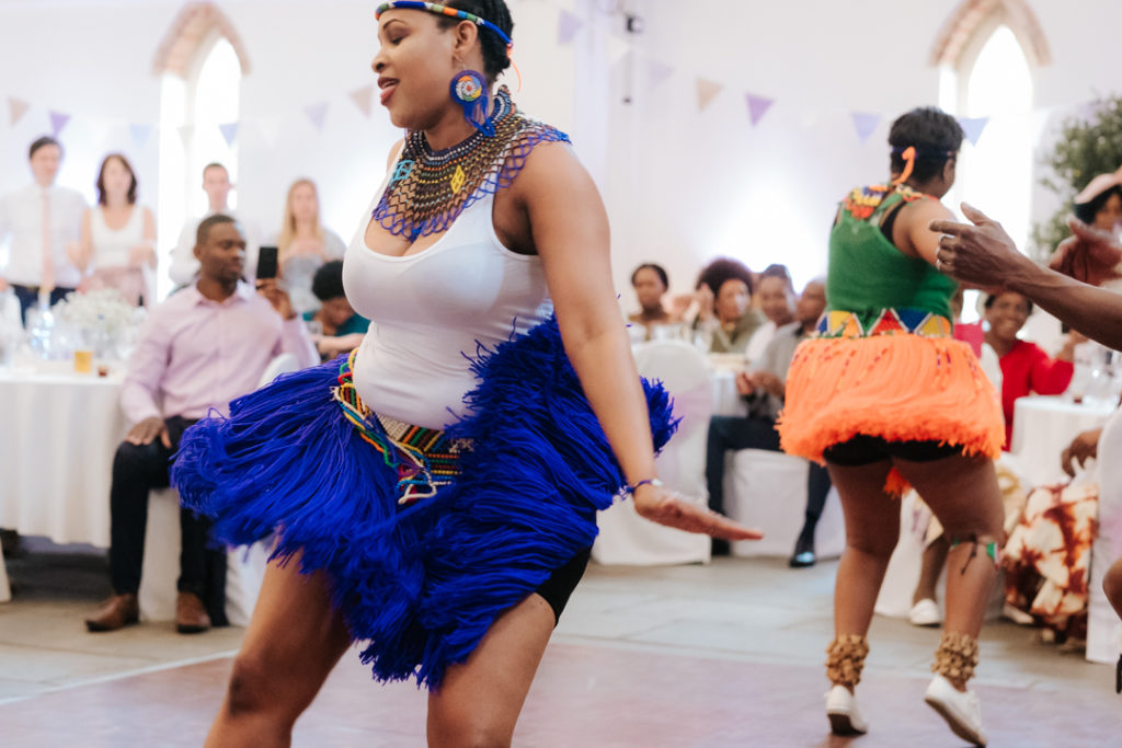 femal african dancers flick thier skirts as they dance at a fusion wedding at Worton hall wedding venue