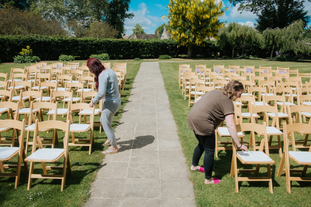 Bridesmaids laying decorations on seats in Worton Hall's outdoor garden wedding green