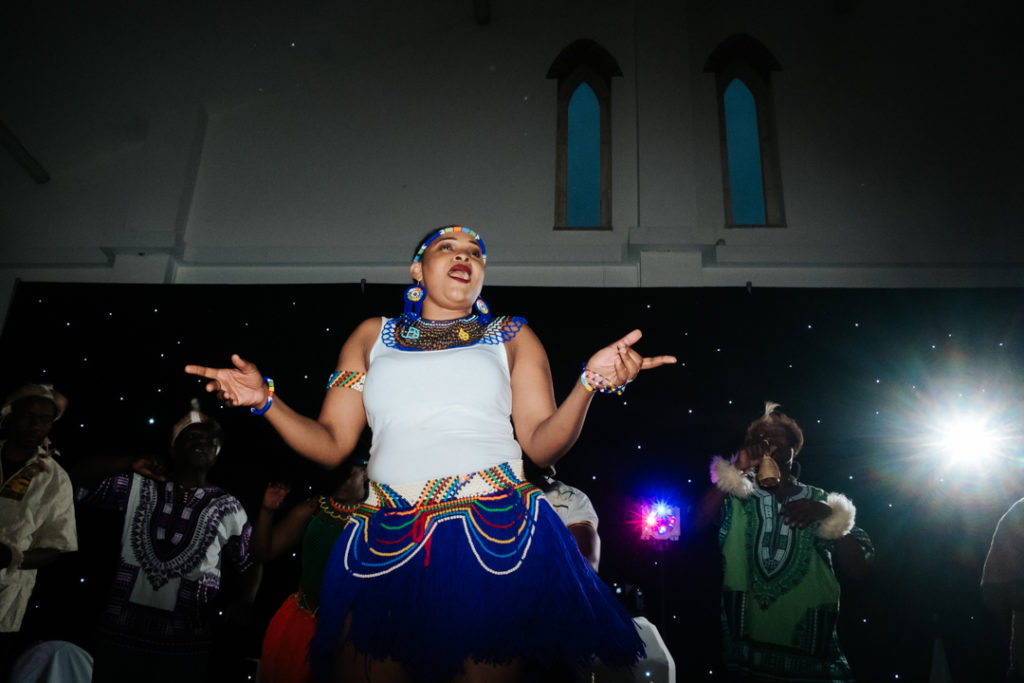 female african dancer sings as she dances to the drummers at a fusion wedding at Worton hall wedding venue