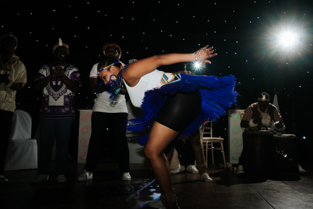 female african dancer flicks her skirt backwards as she dances to the drummers at a fusion wedding at Worton hall wedding venue