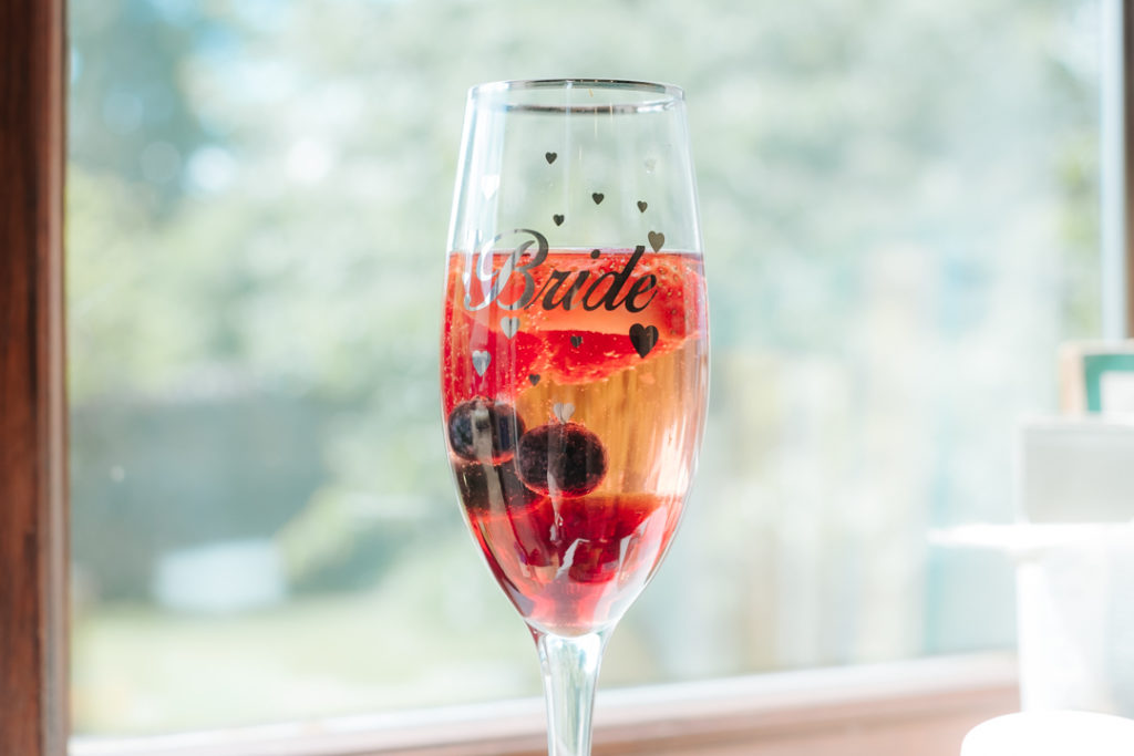 Glass of champagne with "bride" printed on the outside, filled with red berries and champagne at Worton Hall wedding venue