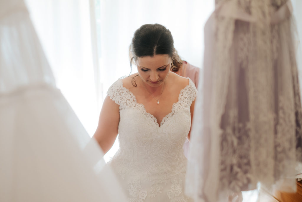 Bride looking downwards as she gets into her wedding dress at Worton Hall wedding venue