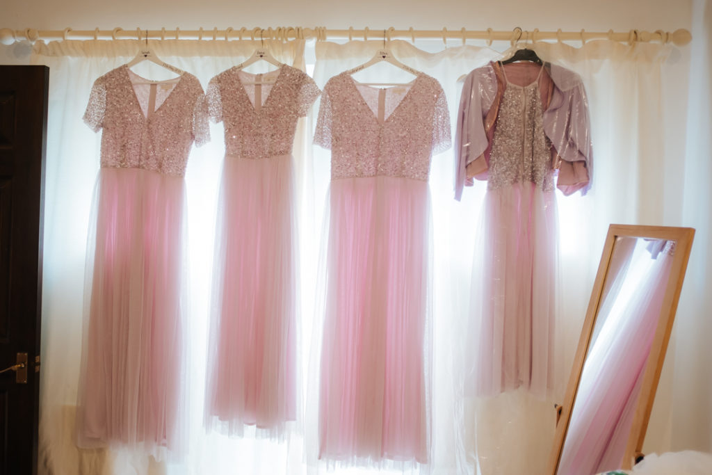 4 pink bridesmaids dresses hanging in the window at Worton Hall wedding venue on the morning of Rachel and Godwin's wedding