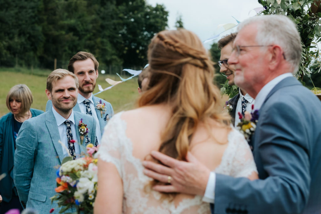 the moment the groom first catches the eye of his bride after she walks down the field pathway to their relaxed festival wedding ceremony at Hasdham farm weddings