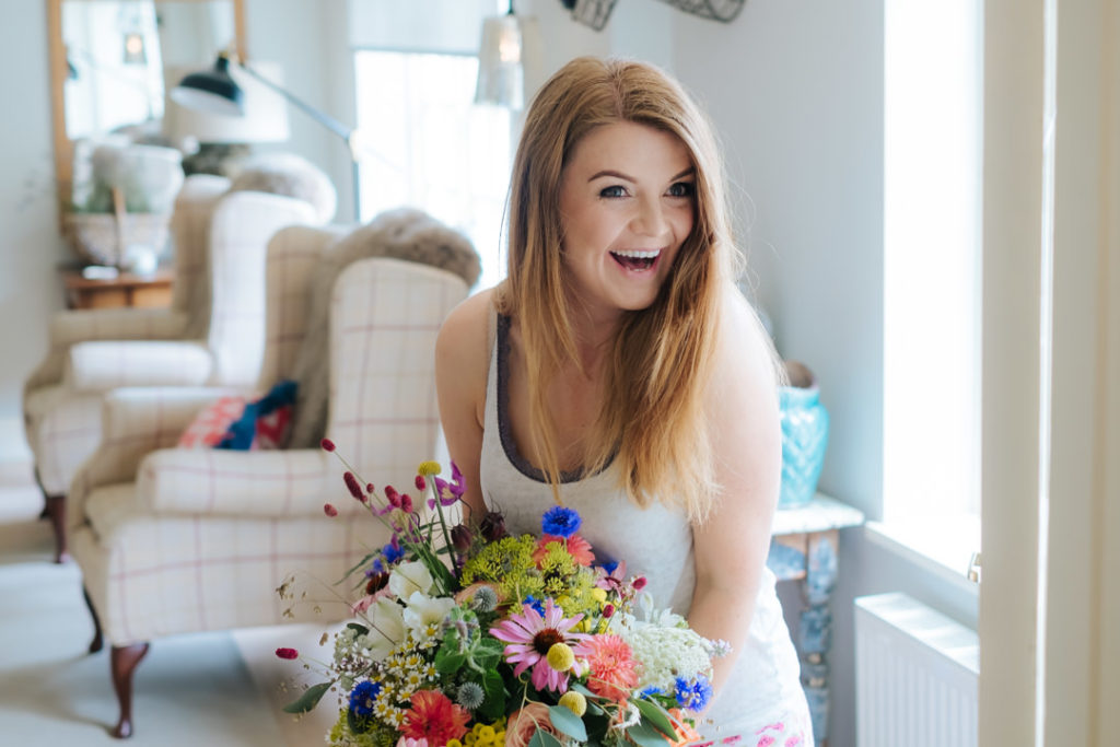 Bride to be holds her wedding bouquet designed by Meadow Dreams Florist and smiles with joy. The bouquet contains wild wedding flowers including pink, blue, green, yellow and red flowers