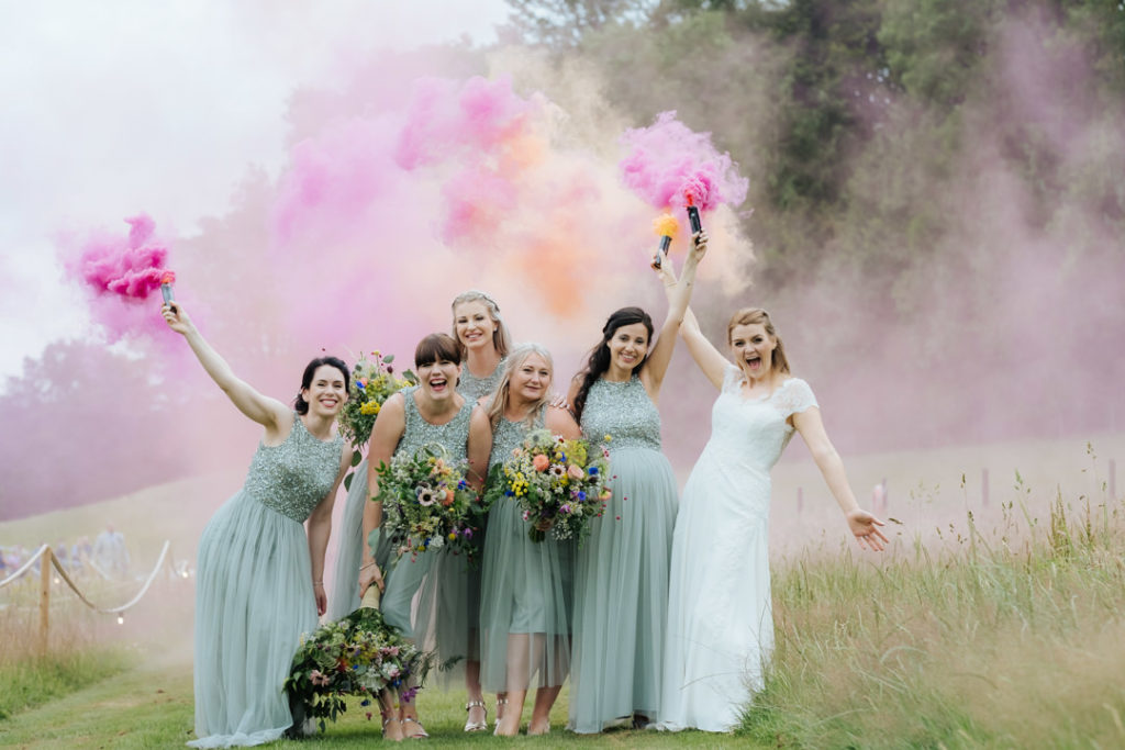 bride and bridesmaids stand together at Hadsham Farm Weddings with pink and orange smoke bomb flares