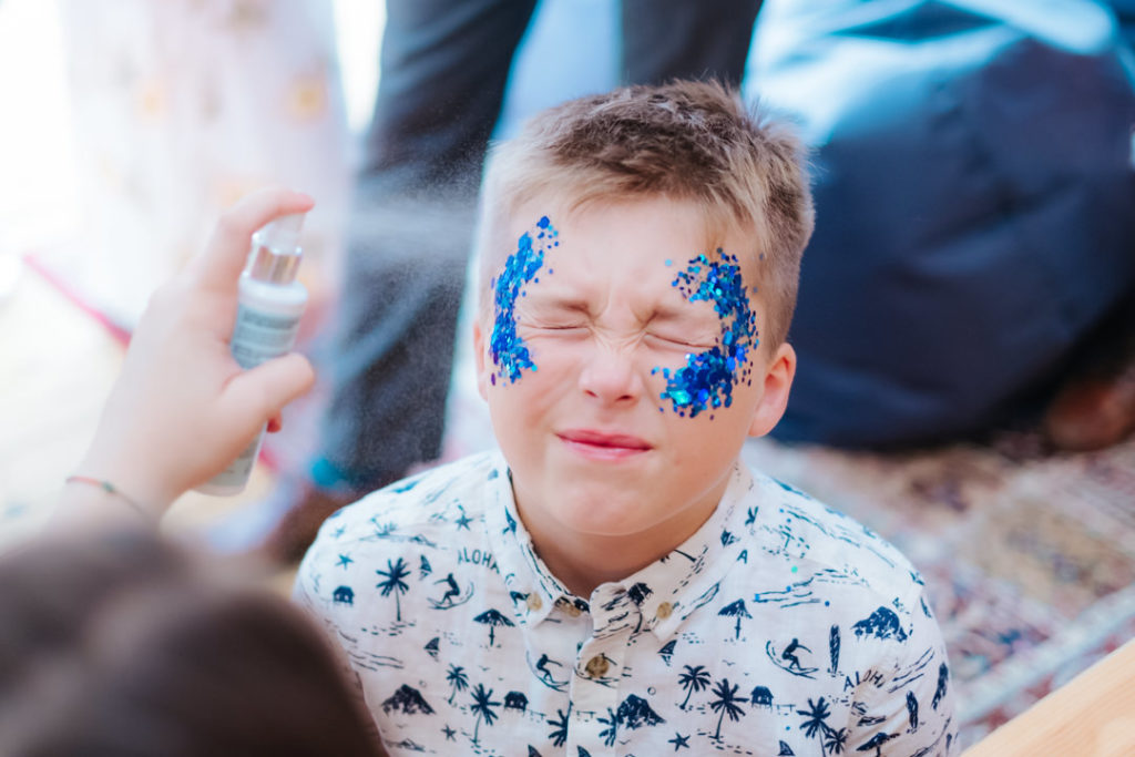 young boy blue glitter applied to his face at Hadsham farm tipi festival wedding in banbury, fun and relaxed wedding photography was the order for this day