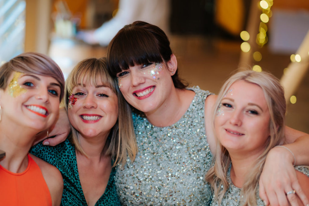 A group of 4 femal friends hug and smile as they pose for a photo on the tipi dancefloor at hadsham farm weddings, Banbury