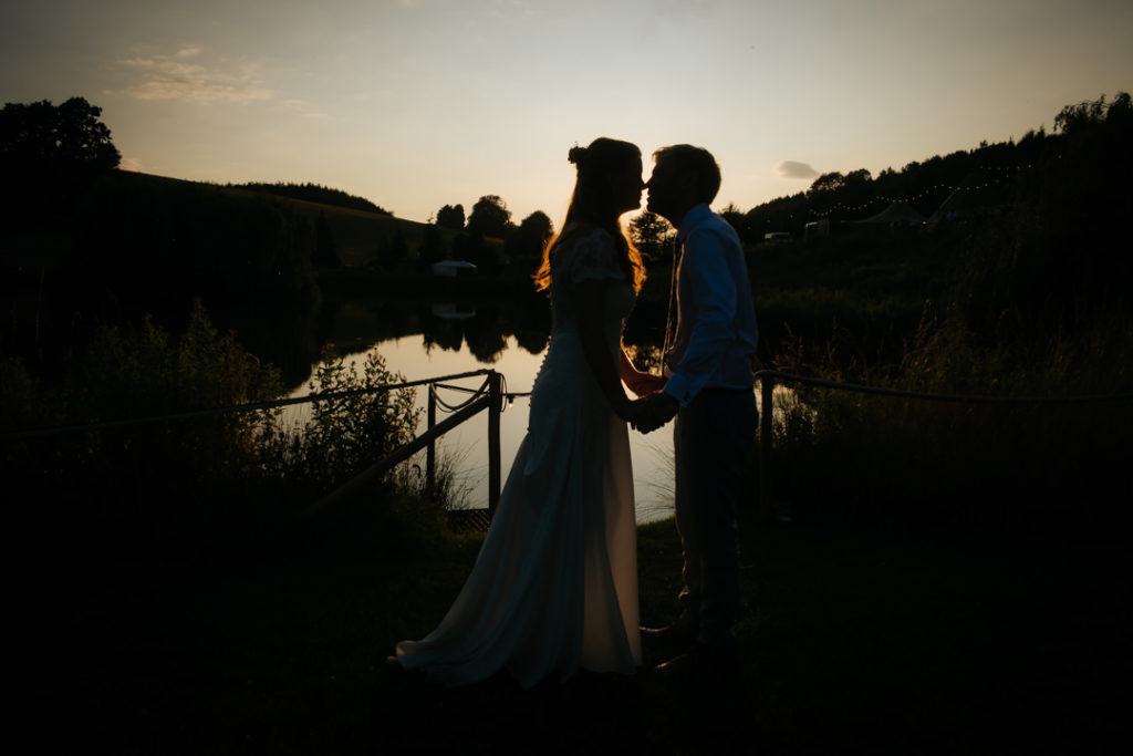 silhouette of bride and groom kissing at sunset in front of the lake at Hadsham Farm weddings, Banbury.