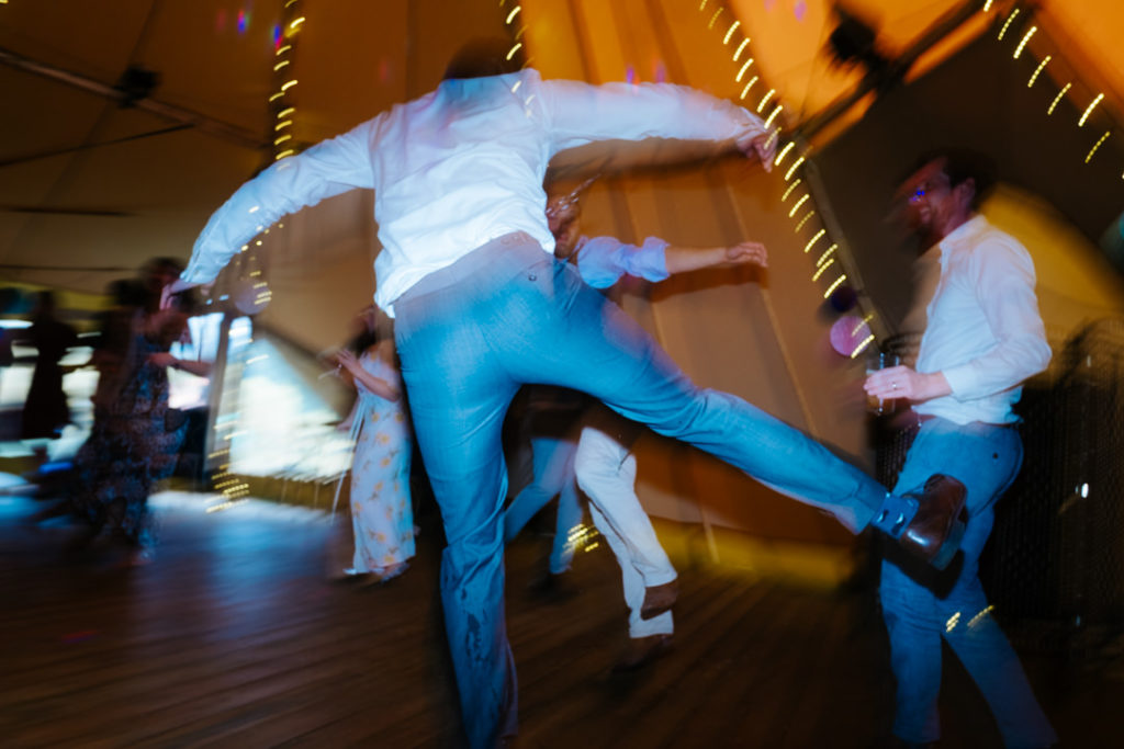 3 men dancing in the tipi at Hadsham farm weddings. One jumps in the air to the beat of the music