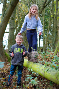 Children in the woods balancing on a log smiling and giving thumbs up