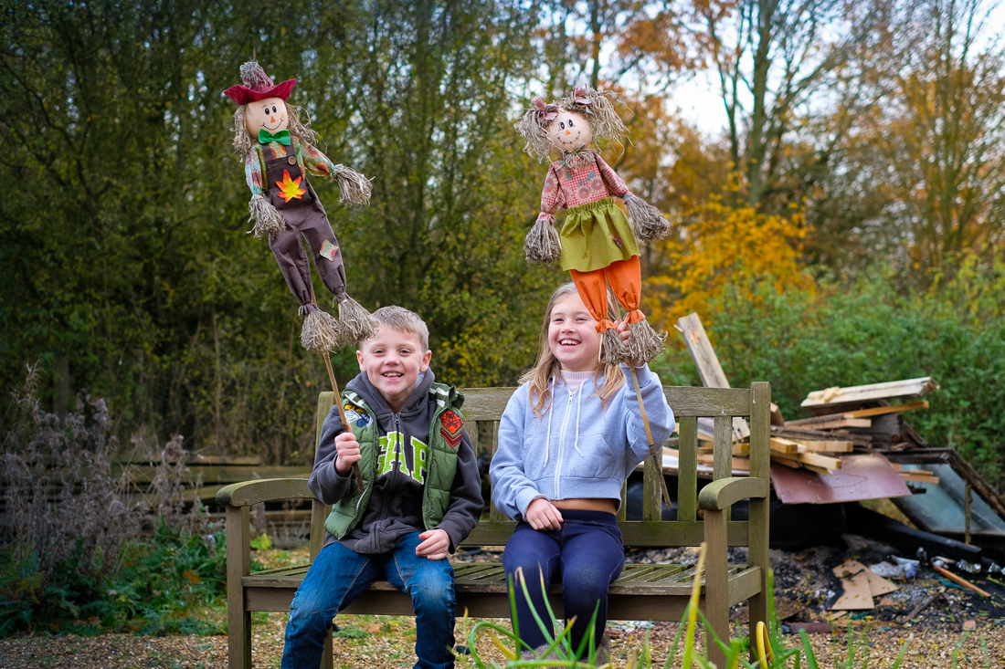 Children sitting on garden bench smiling as they show off their homemade scarecrows