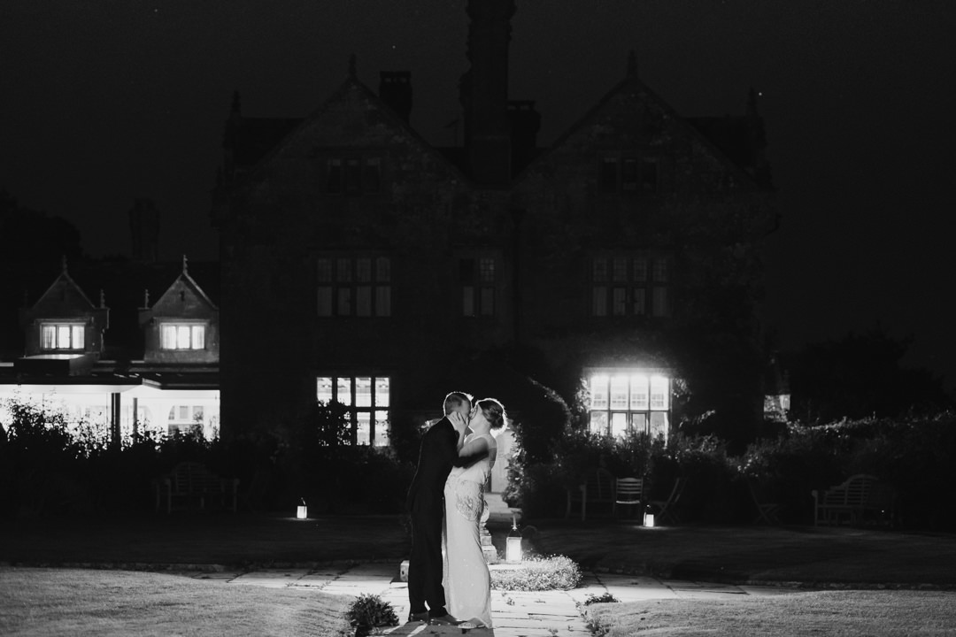 Bride and groom kiss in the dark outside the house at Gravetye Manor. backlit photograph