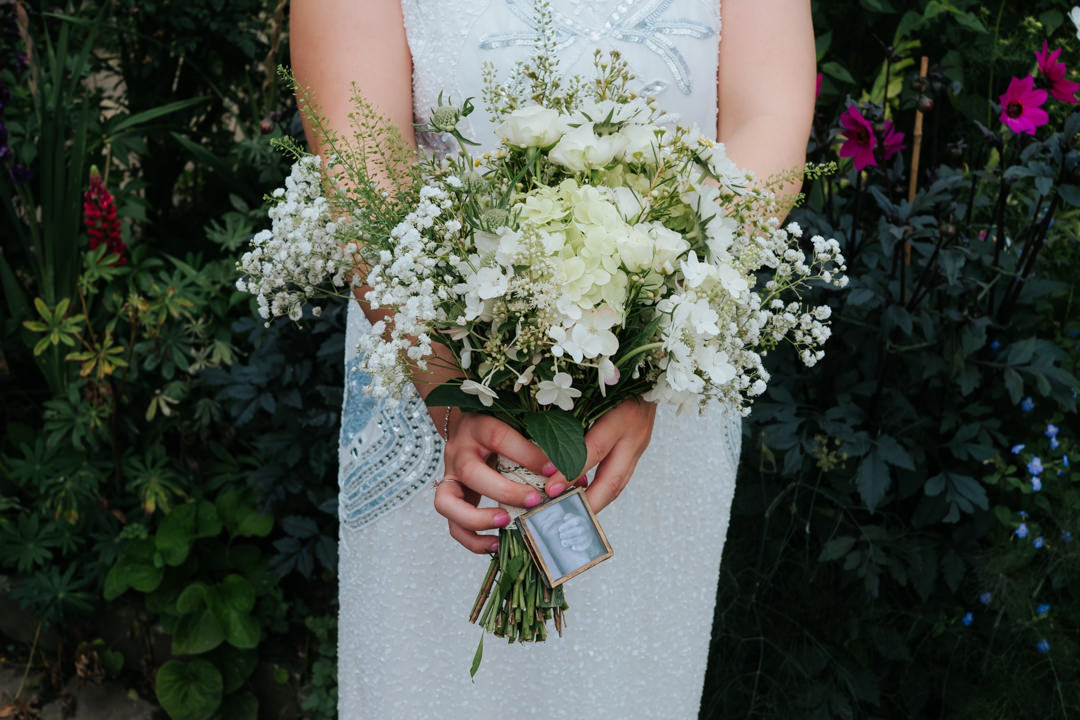 Bride holds out her bouquet at Gravetye Manor. Beautiful cream and green wedding flowers containing roses