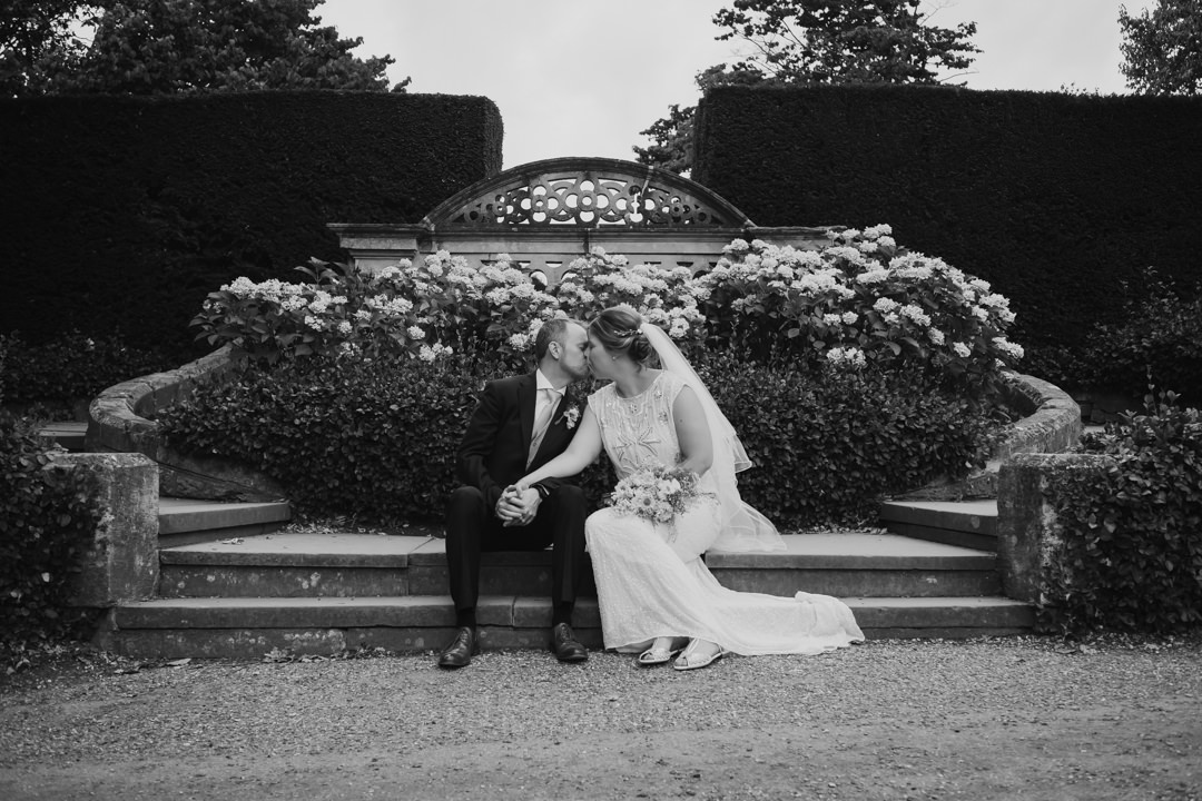 Bride and groom kiss beneath beautiful cream flowers after their wedding at Nymans Gardens