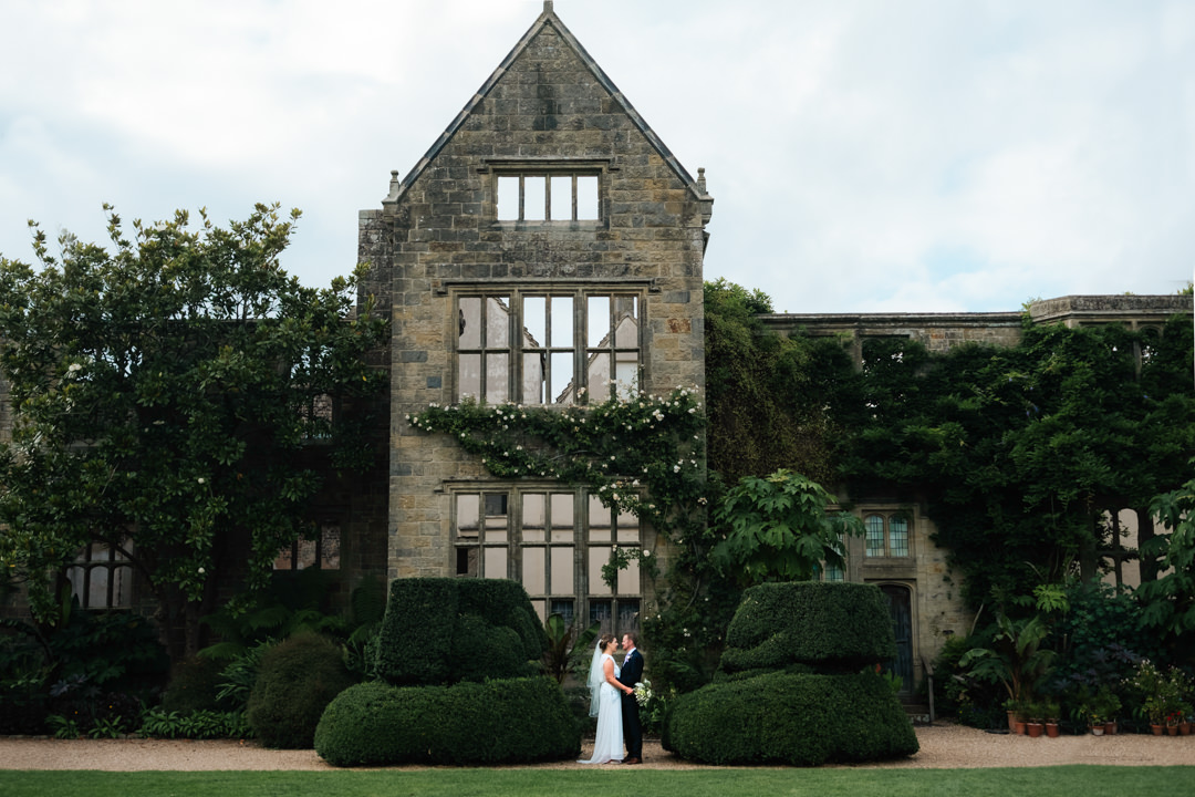 Small bride and groom stnad together beneath huge beautiful relic of the house at Nymans Gardens afer getting marries in the sunk Garden
