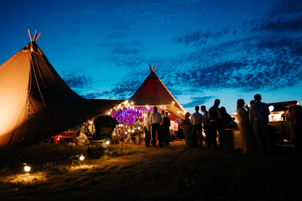 Wedding tipi glowing in the dusk sky as the amazing sunset shows off bright blue clouds in the background 