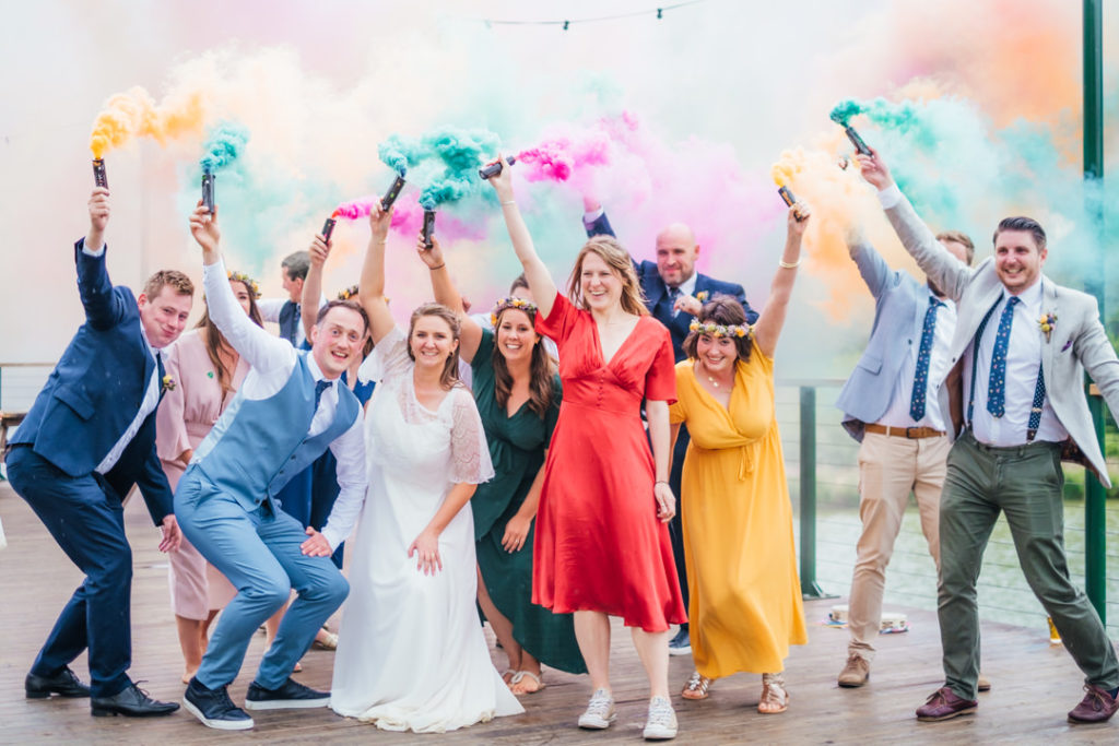 bride and groom with thier friends holding coloured smoke flares on thier wedding day at Hadsham Farm banbury