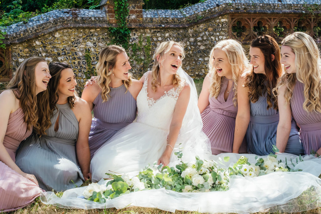 pastel coloured bridesmaids sitting down laughing with bride photographed by devon wedding photographer Charlie Flounders